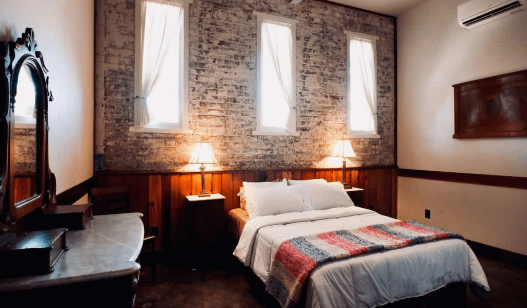 A ruler bed in a visitor room with uncovered brick dividers and collectible furniture at The Motel at the Ancient Imprison, a lodging in Modern Orleans, Louisiana